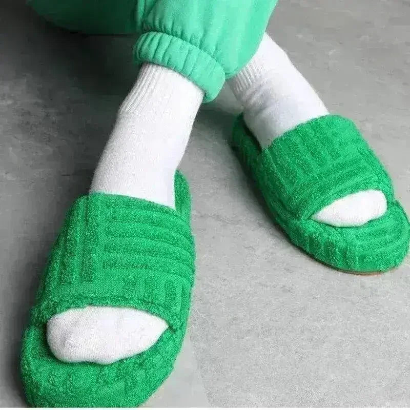 Green fuzzy open-toe slide slippers on feet with white socks.