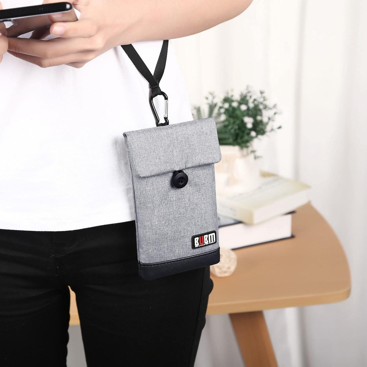 Grey phone pouch worn crossbody with flap and snap closure; phone stored in front pocket