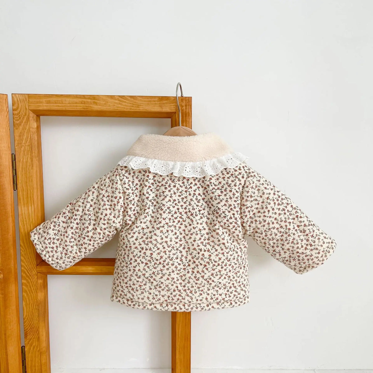 Floral baby winter coat with sherpa collar and long sleeves, hanging on hook