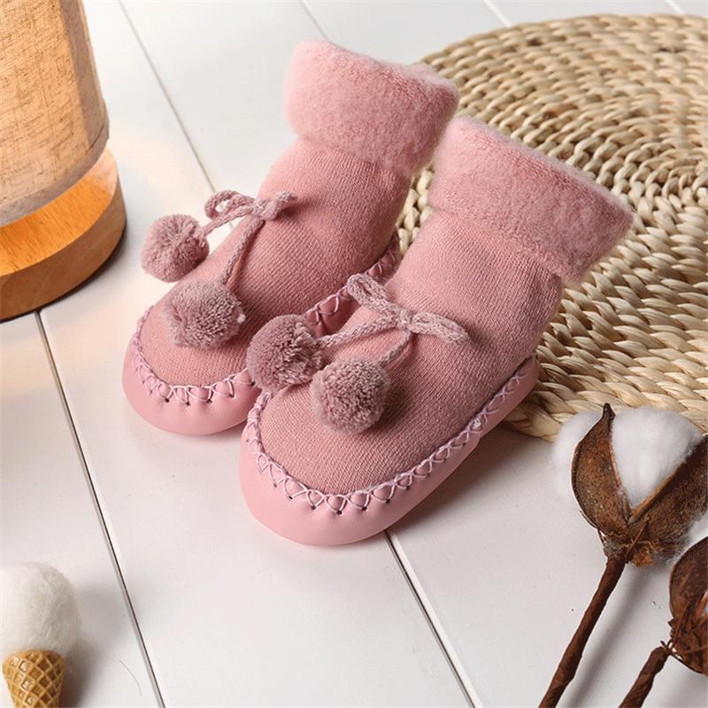 Newborn baby shoes in light pink soft fabric with bow and pom pom accents