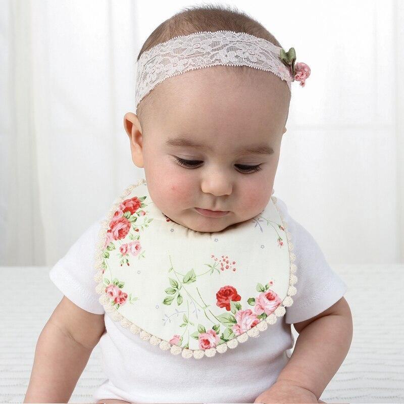 Baby wearing a floral double-layer bib with pom trim and a lace edge