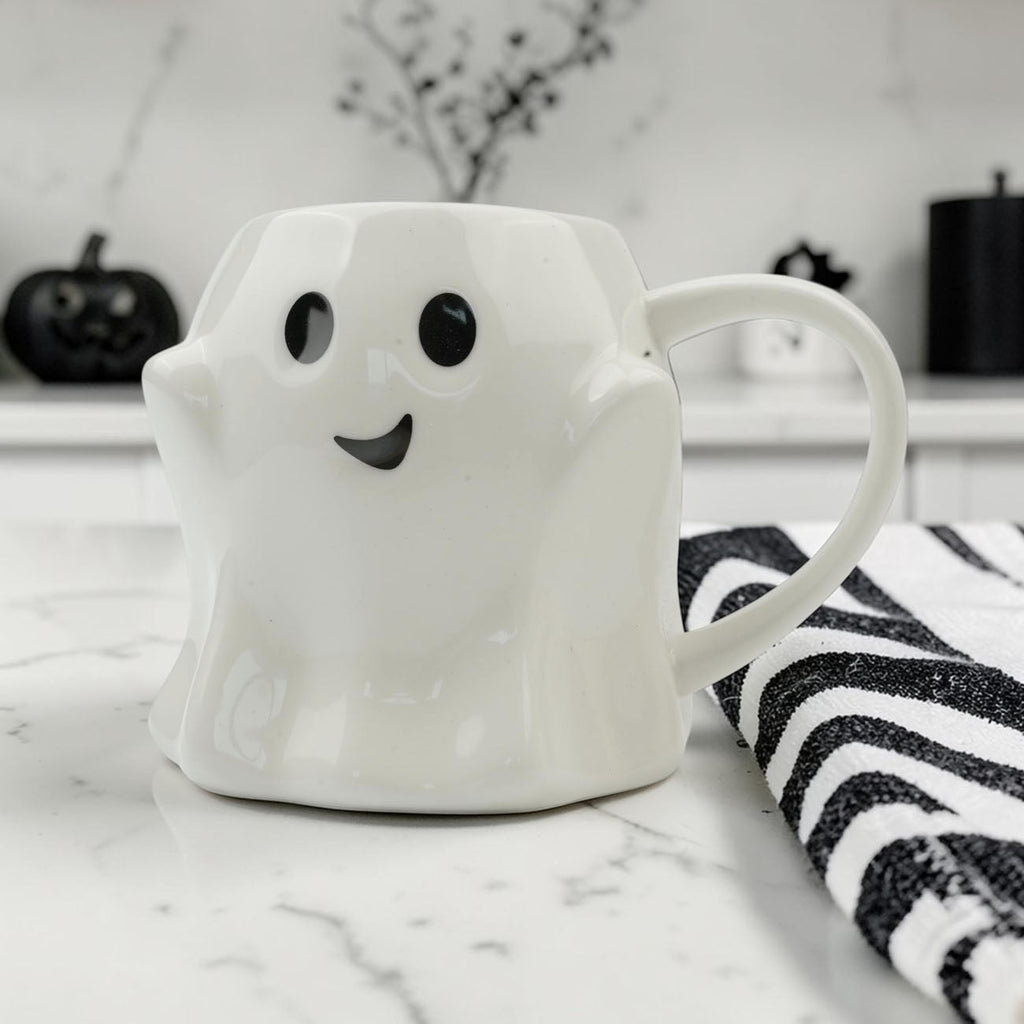 White ghost-shaped mug with black eyes and a curved smile
