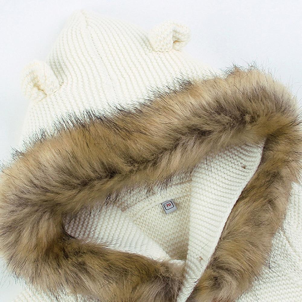 Newborn jacket close-up: white knit hood with tan faux-fur lining and logo patch