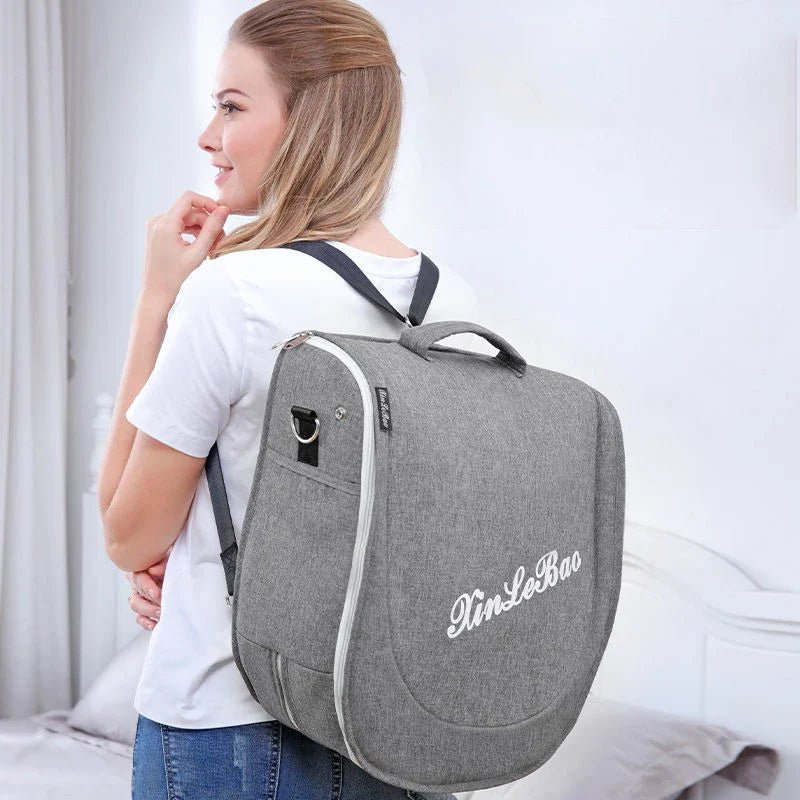 Grey folding baby cot carried with shoulder straps, front logo patch visible