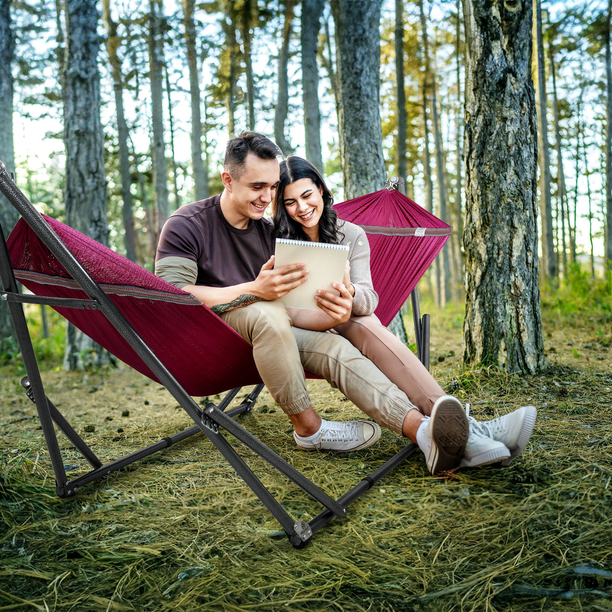 Maroon fabric hammock on black folding stand, with two people relaxing outdoors