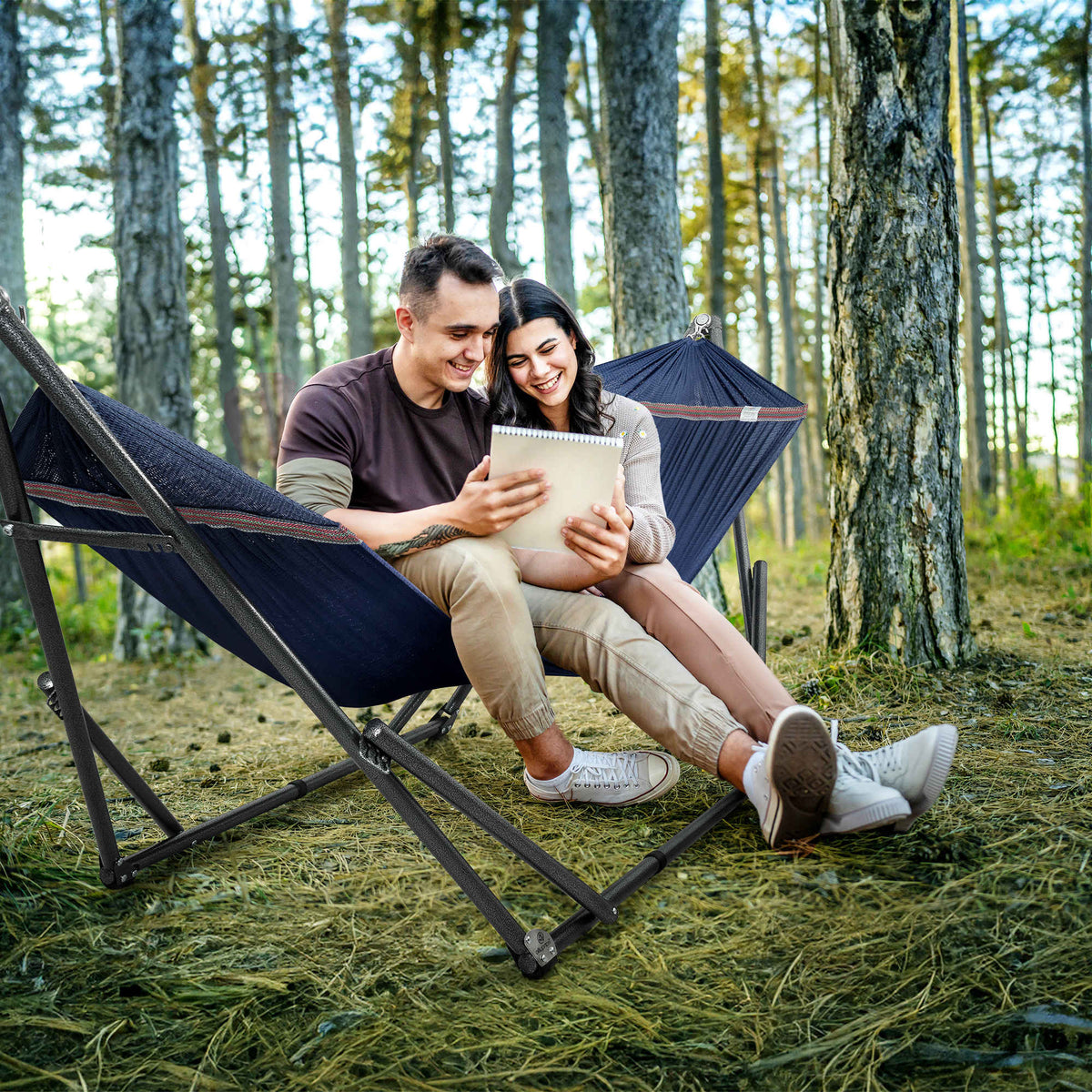 Dark blue hammock on black stand with two people relaxing in a forest
