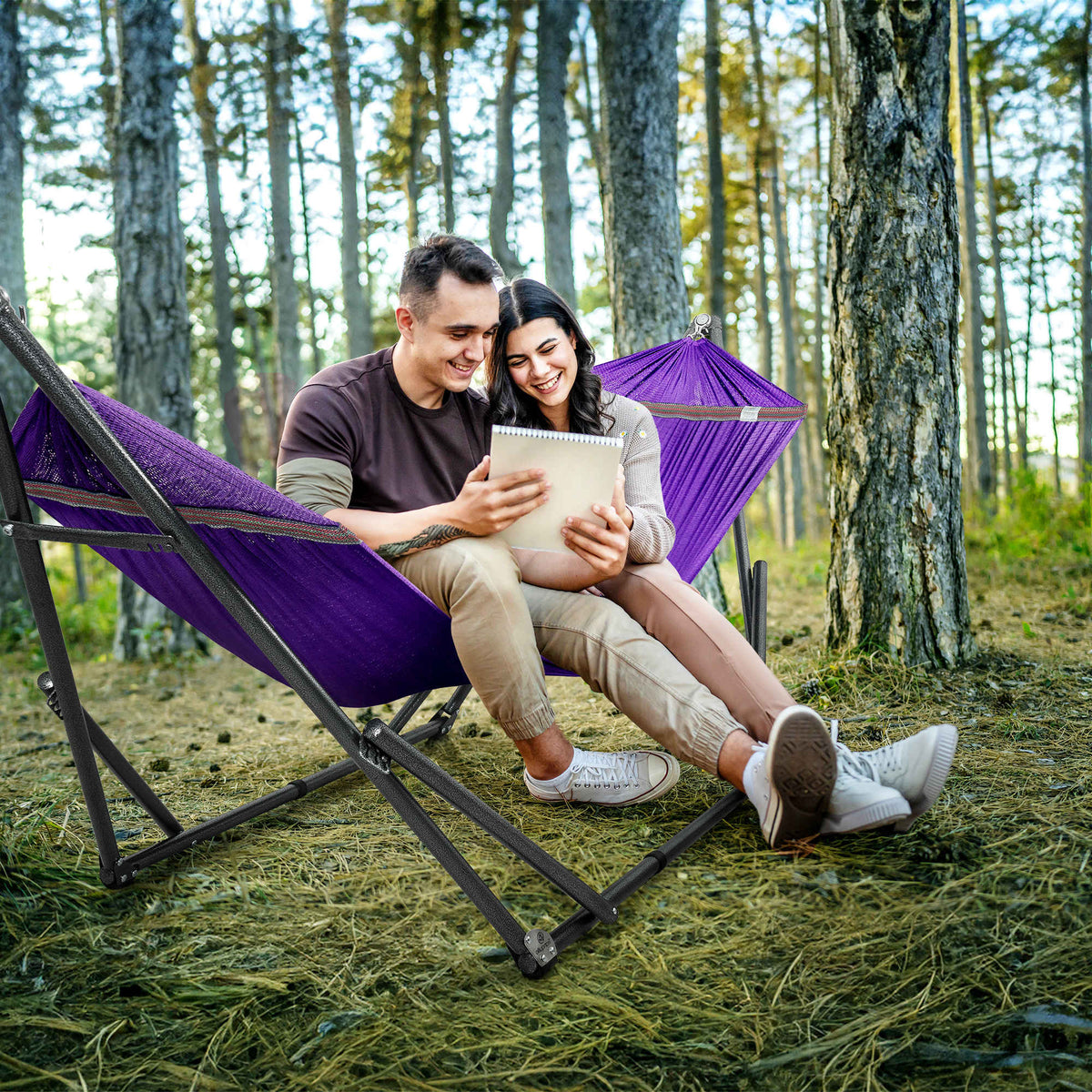 Purple fabric hammock on a black folding stand, holding two people reclining.