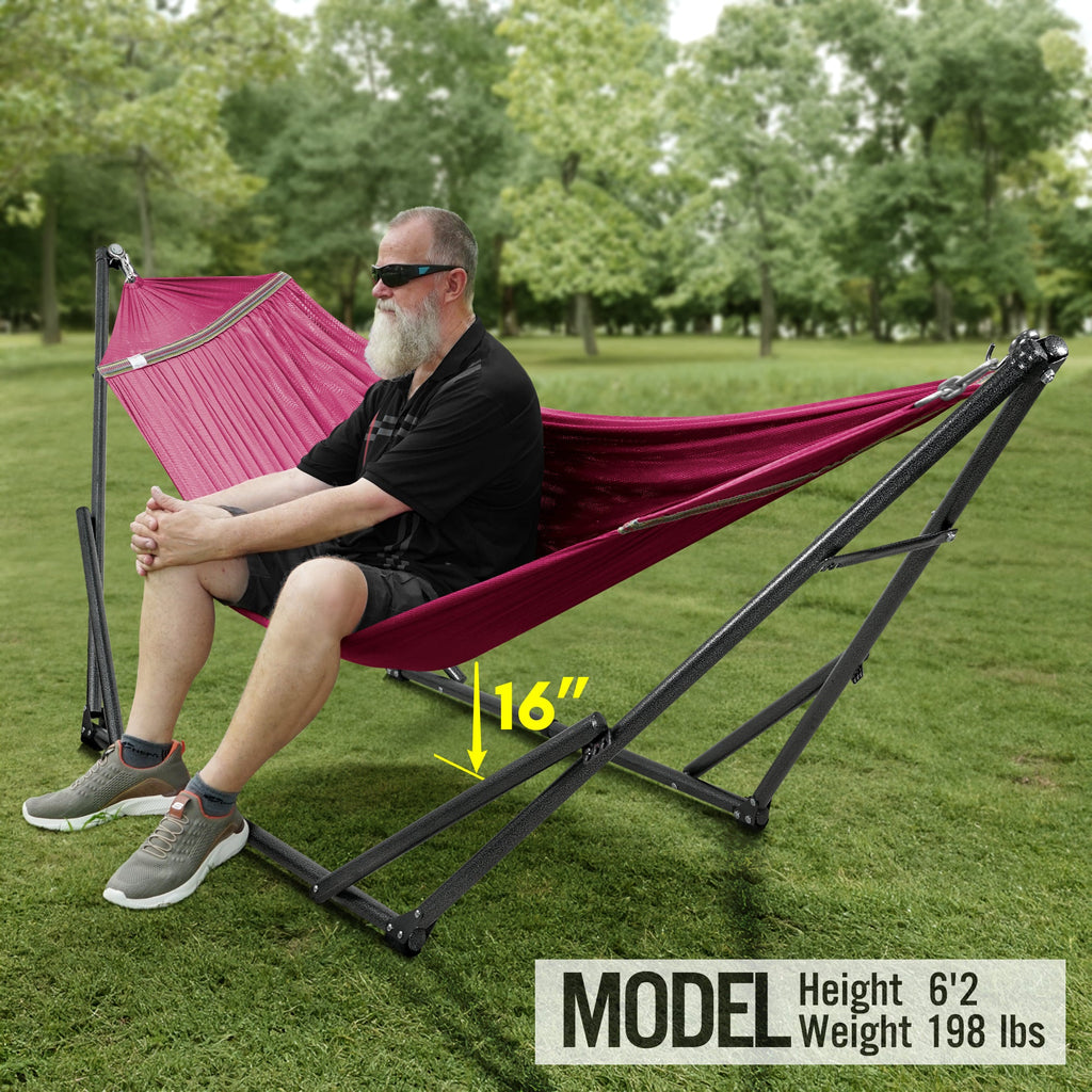 Maroon hammock on a black folding stand, with a person relaxing outdoors.