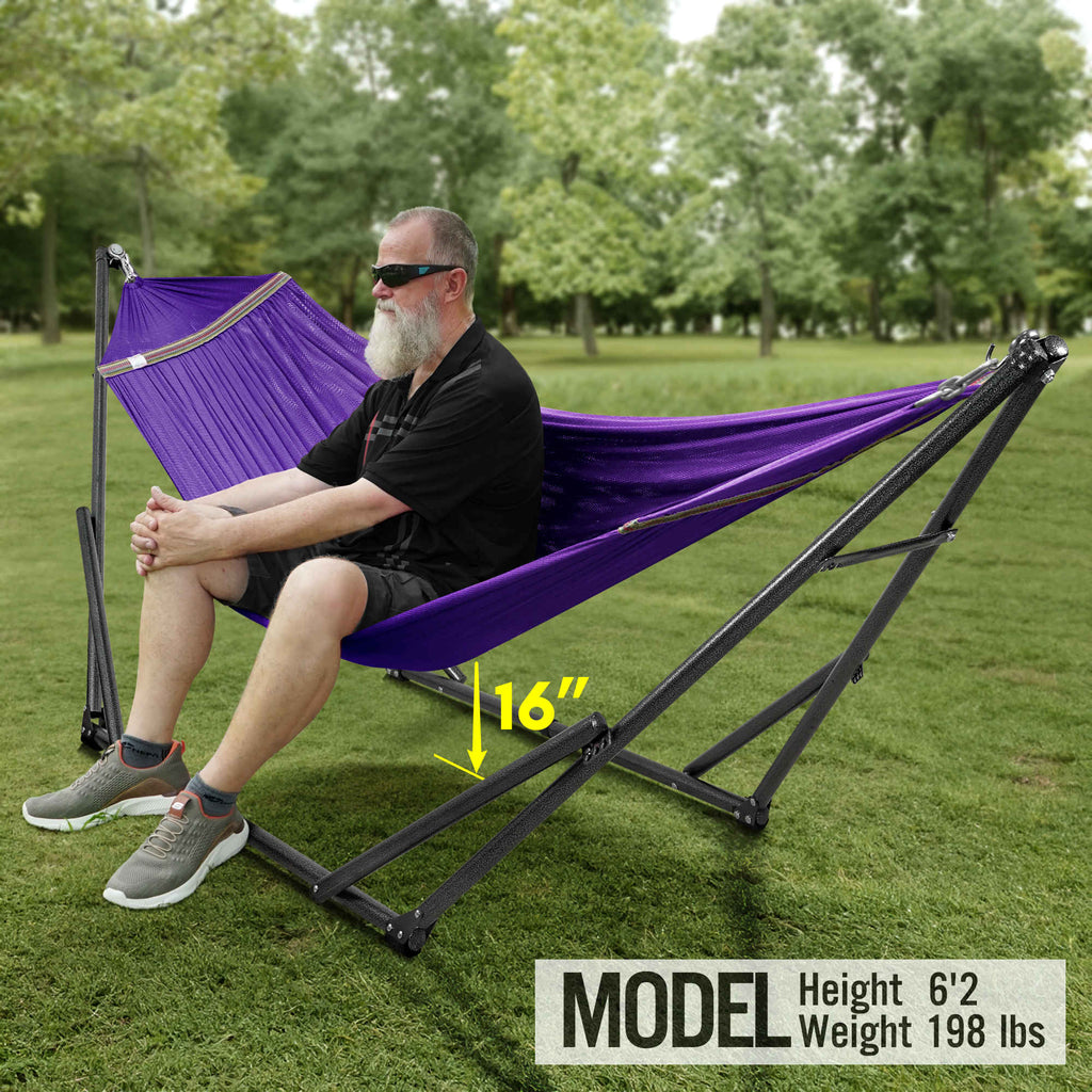Purple hammock on black folding stand with seated person in a grassy park