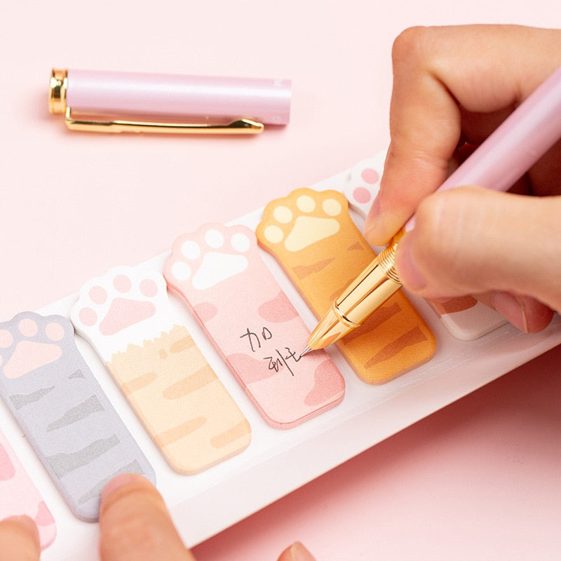 Cat paw sticky notes being placed by hand, with pastel tabs and paw-print shapes