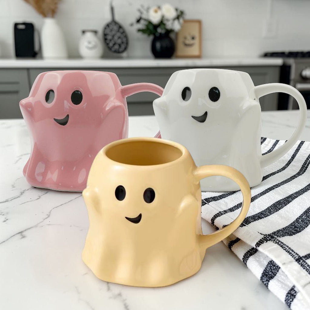 Set of three ghost-shaped ceramic mugs in pink, white, and yellow with handles