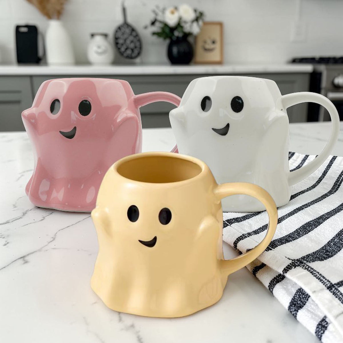 Set of three ghost-shaped ceramic mugs in pink, white, and yellow with handles