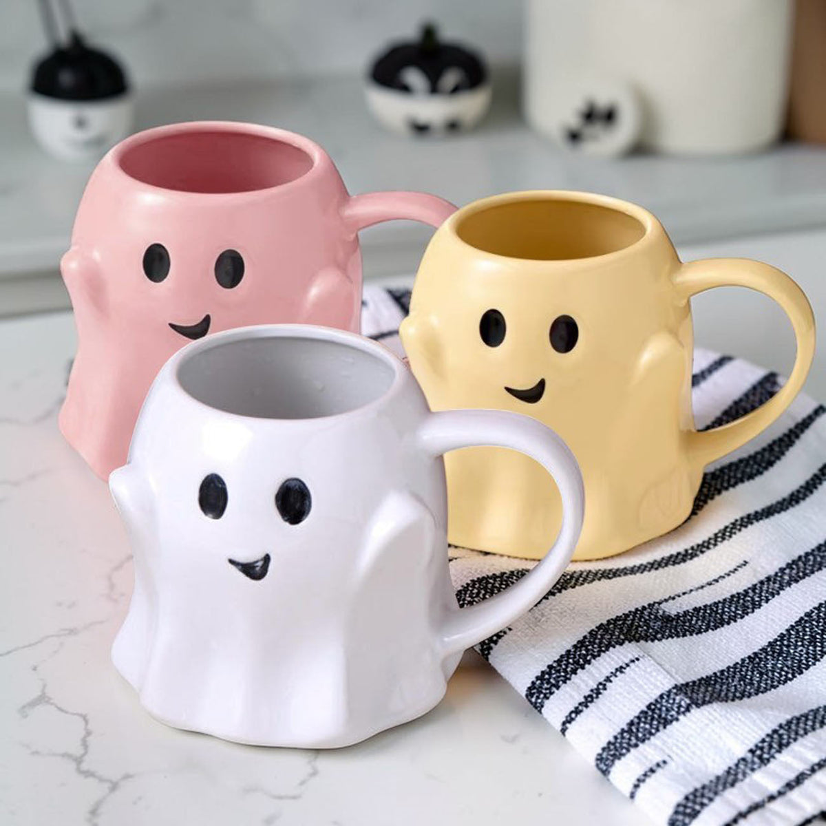 Pink, yellow, and white ghost-shaped ceramic mugs with cute faces and curved handles