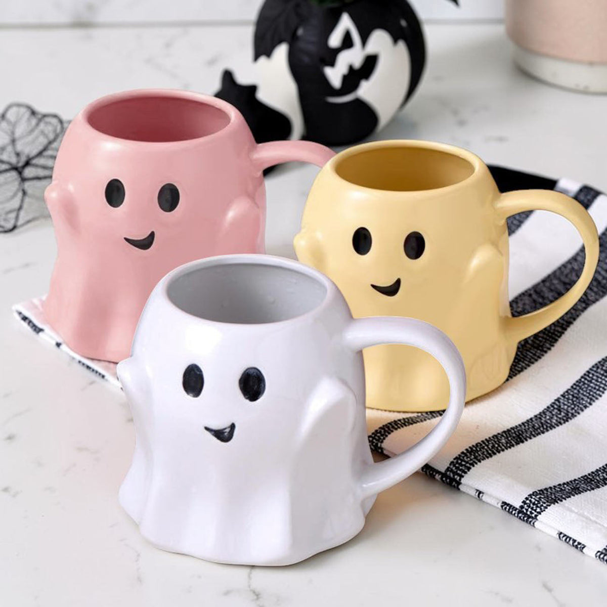 Assorted ghost-shaped mugs in pink, yellow, and white with smiling faces