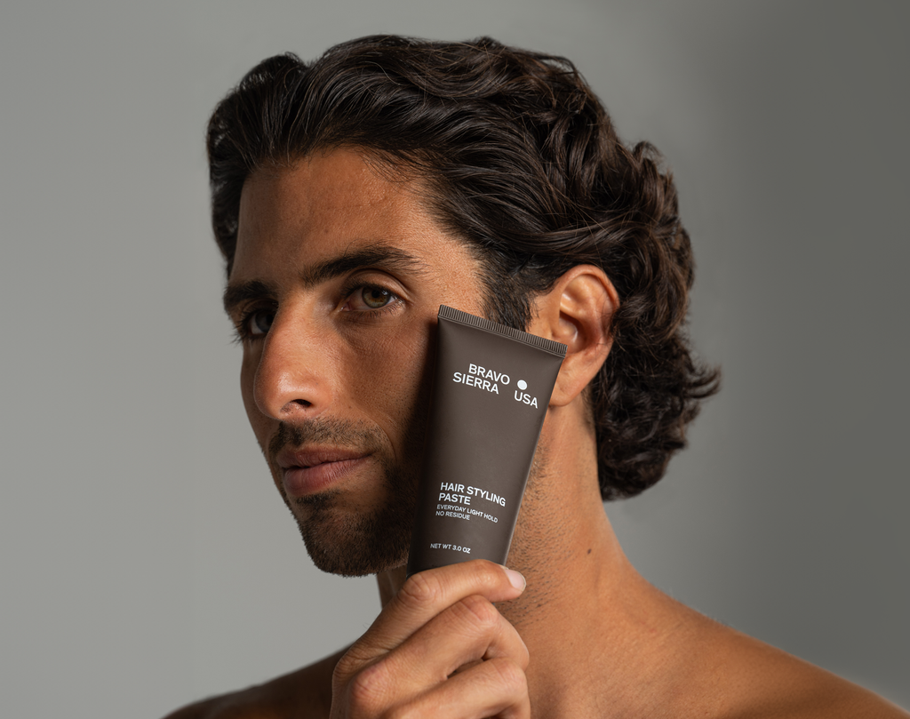 Man holding hair styling paste tube near his face