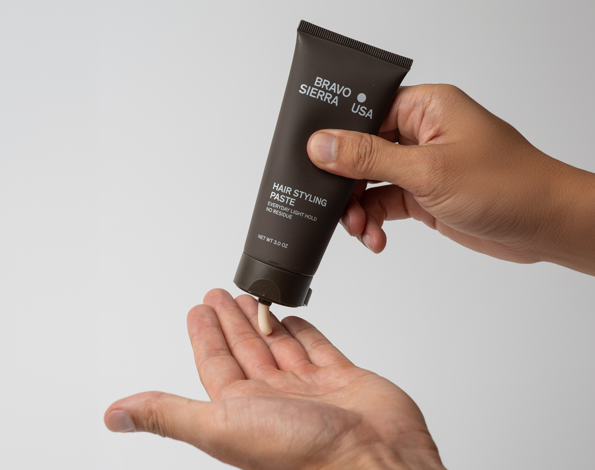 Hand squeezing hair styling paste from brown tube onto open palm