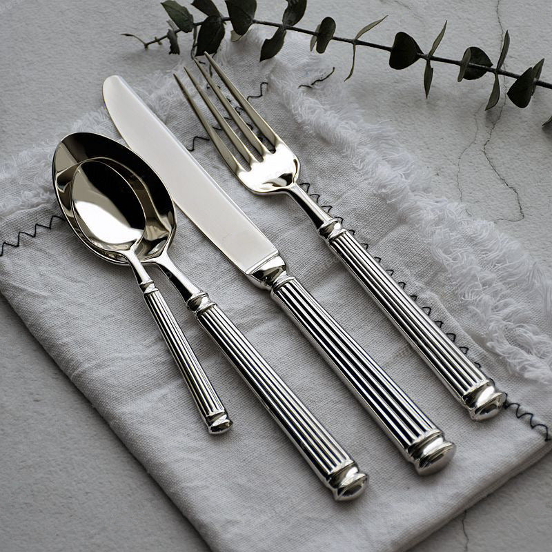 Polished stainless steel Roman-column flatware: spoon, forks, and knife on gray cloth