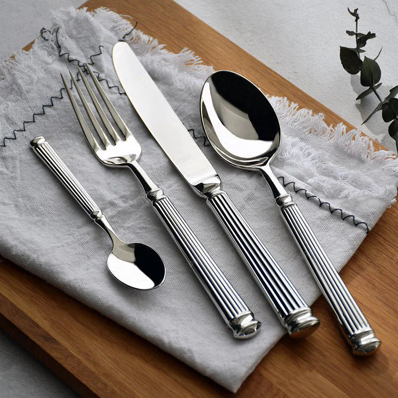 Stainless steel flatware set with Roman-column handles: spoon, fork, and knife on cloth