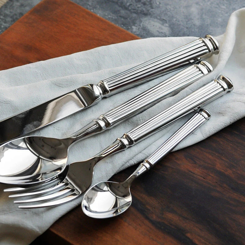 Polished stainless steel spoon, fork, and knife with Roman-column handles on cloth