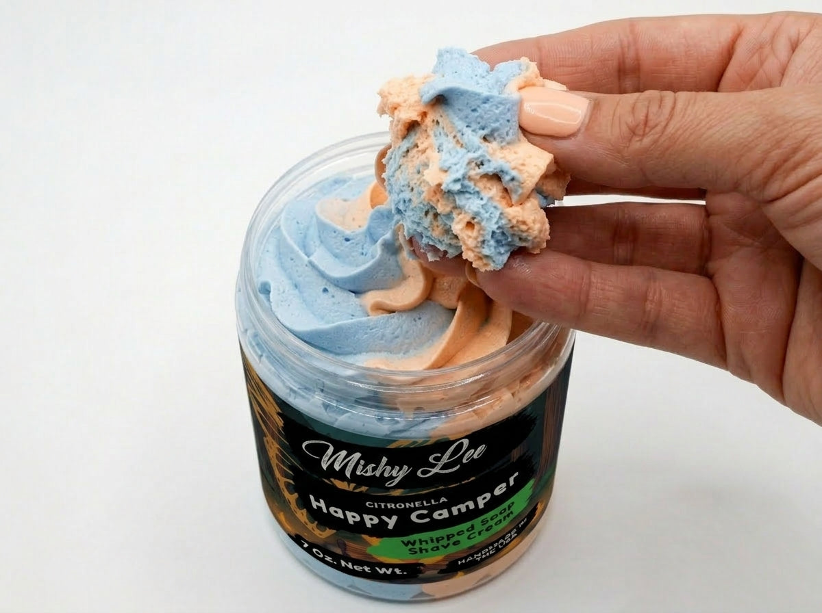Hand holding a blue and peach whipped soap scoop from a Happy Camper jar
