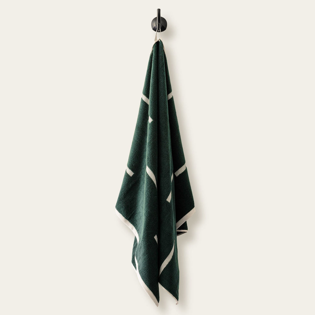 Verdant green cotton towel hanging from hook, ecru stripe border visible