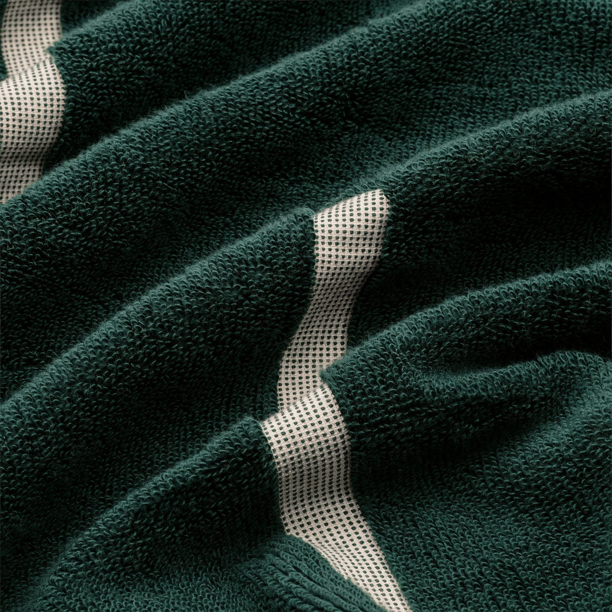 Close-up of verdant green cotton towel with ecru stripe accents on terry texture