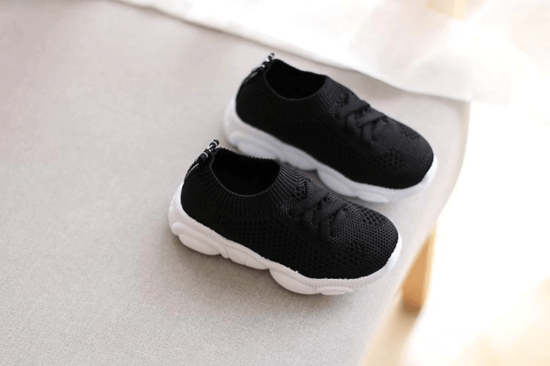 Pair of black knit baby sneakers on a sofa edge with cushioned white soles