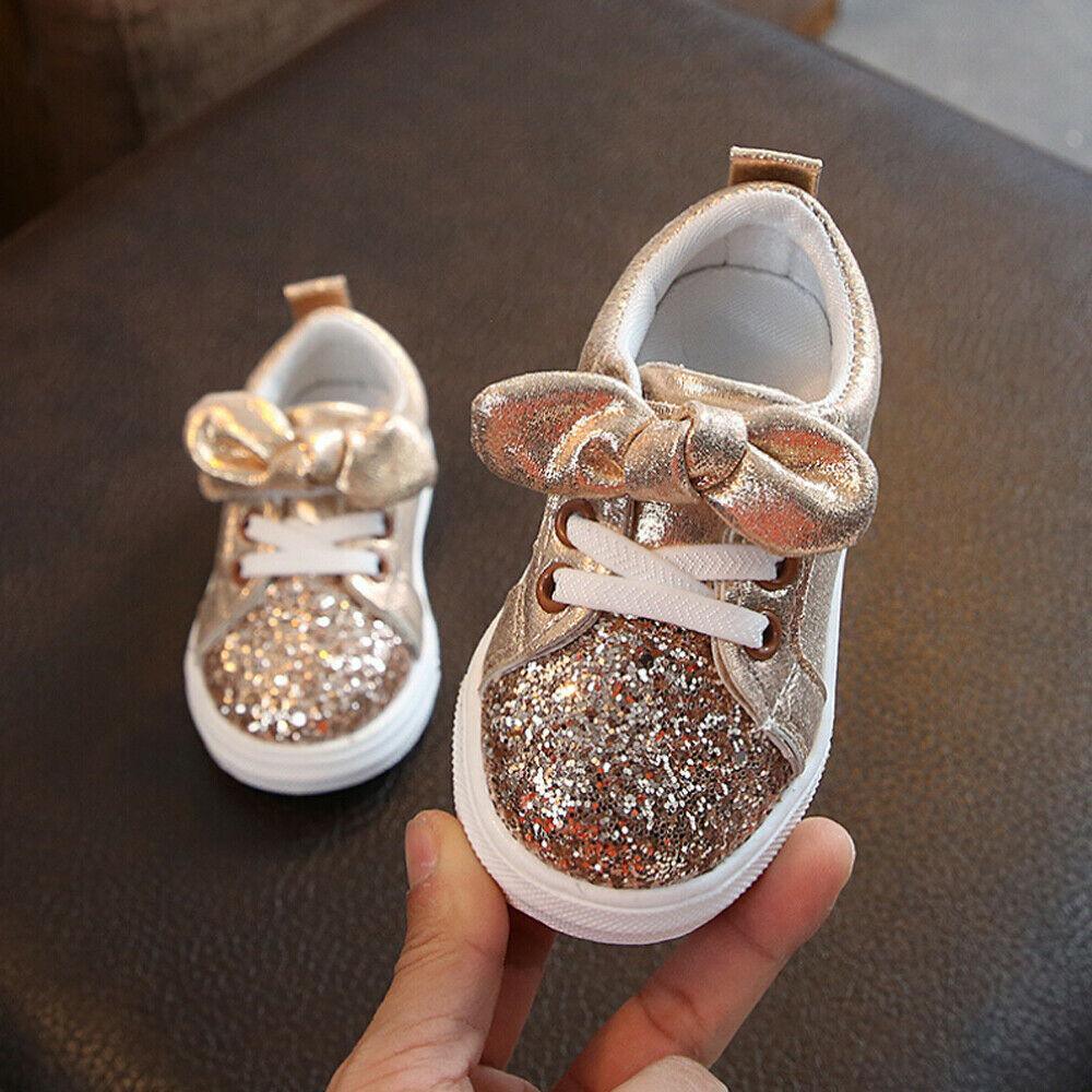 Toddler gold glitter sneakers with bow detail, lace-up, white rubber sole.