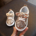 Toddler gold glitter sneakers with bow detail, lace-up, white rubber sole.