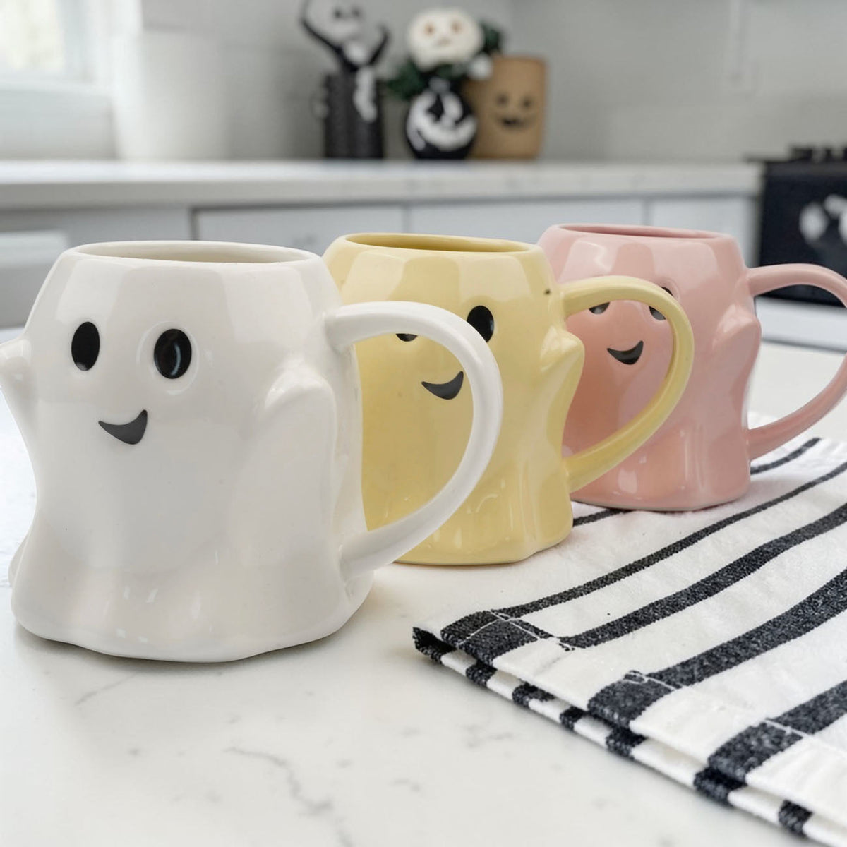 Ghost mugs in white, yellow, and pink lined up on a striped cloth