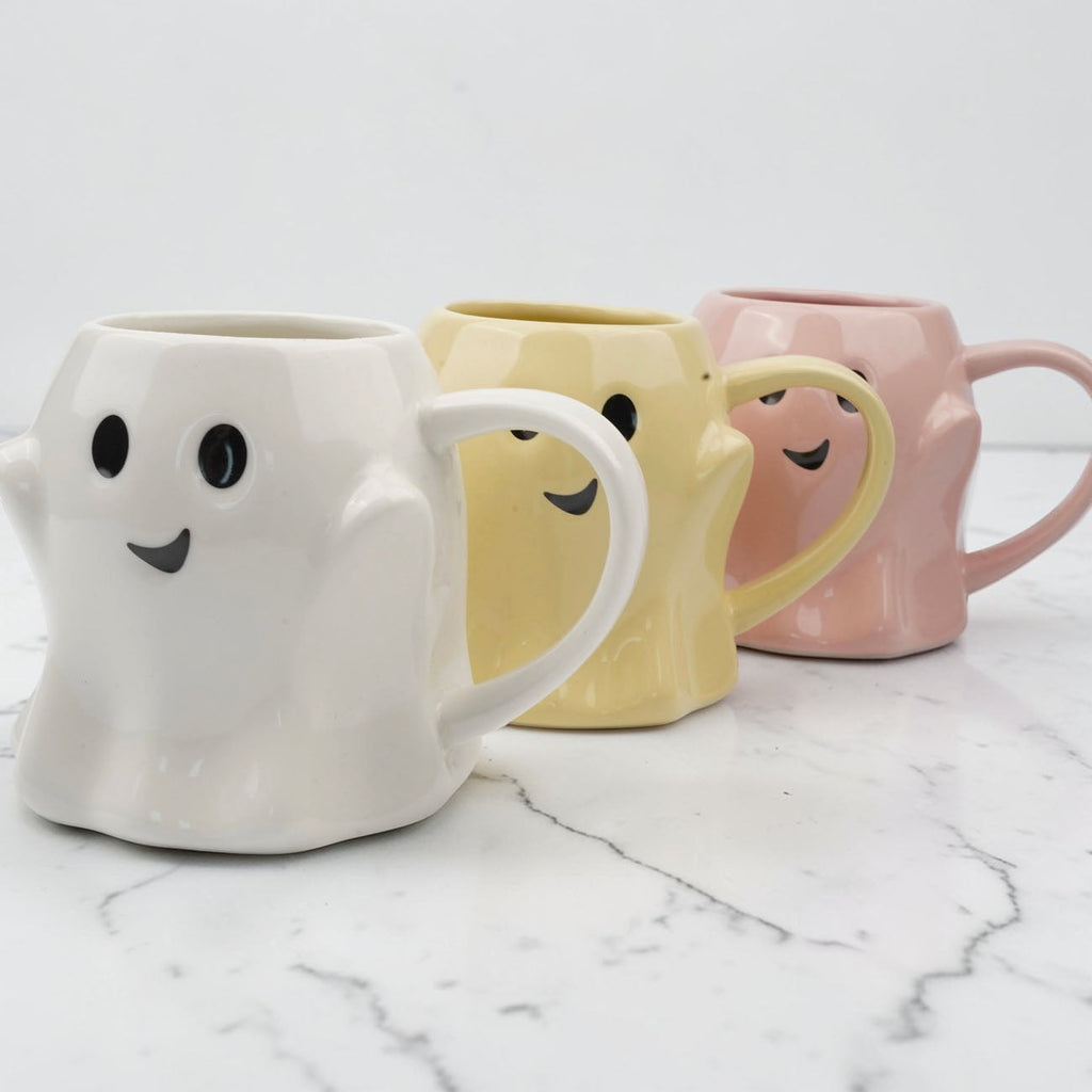 Ghost-shaped ceramic mugs in white, yellow, and pink with smiling faces and handles