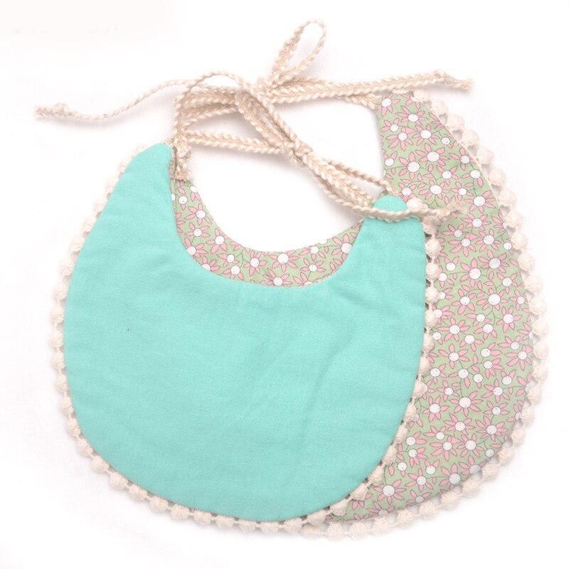 Baby bib set with teal solid front and pink floral back, pom-pom trimmed edges
