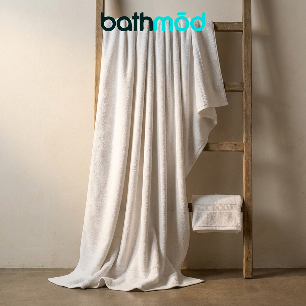 Two white bath sheets, one draped over a wooden stand with a folded towel