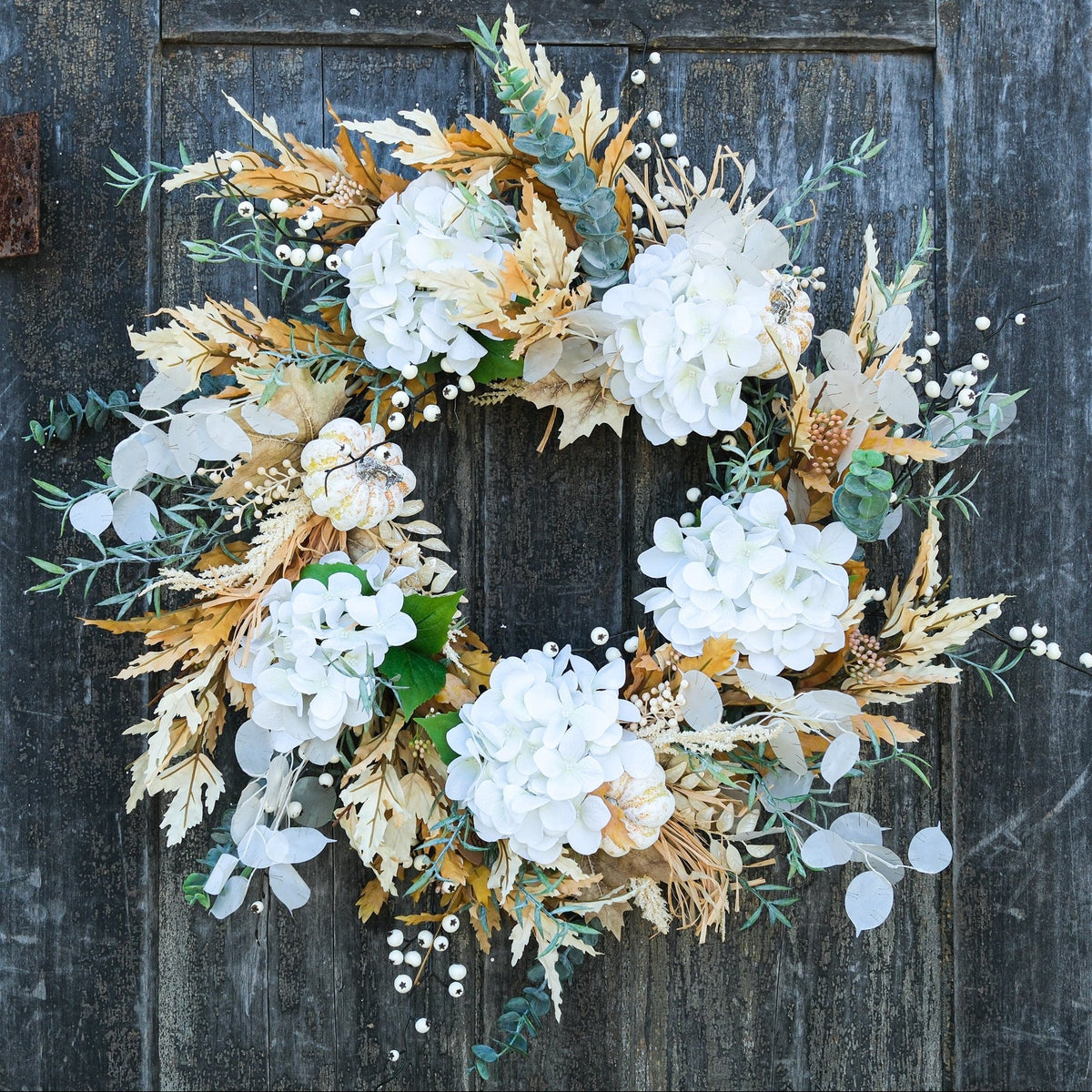 Truffle wreath with white hydrangea blooms, gold leaves, eucalyptus, and small berry accents.