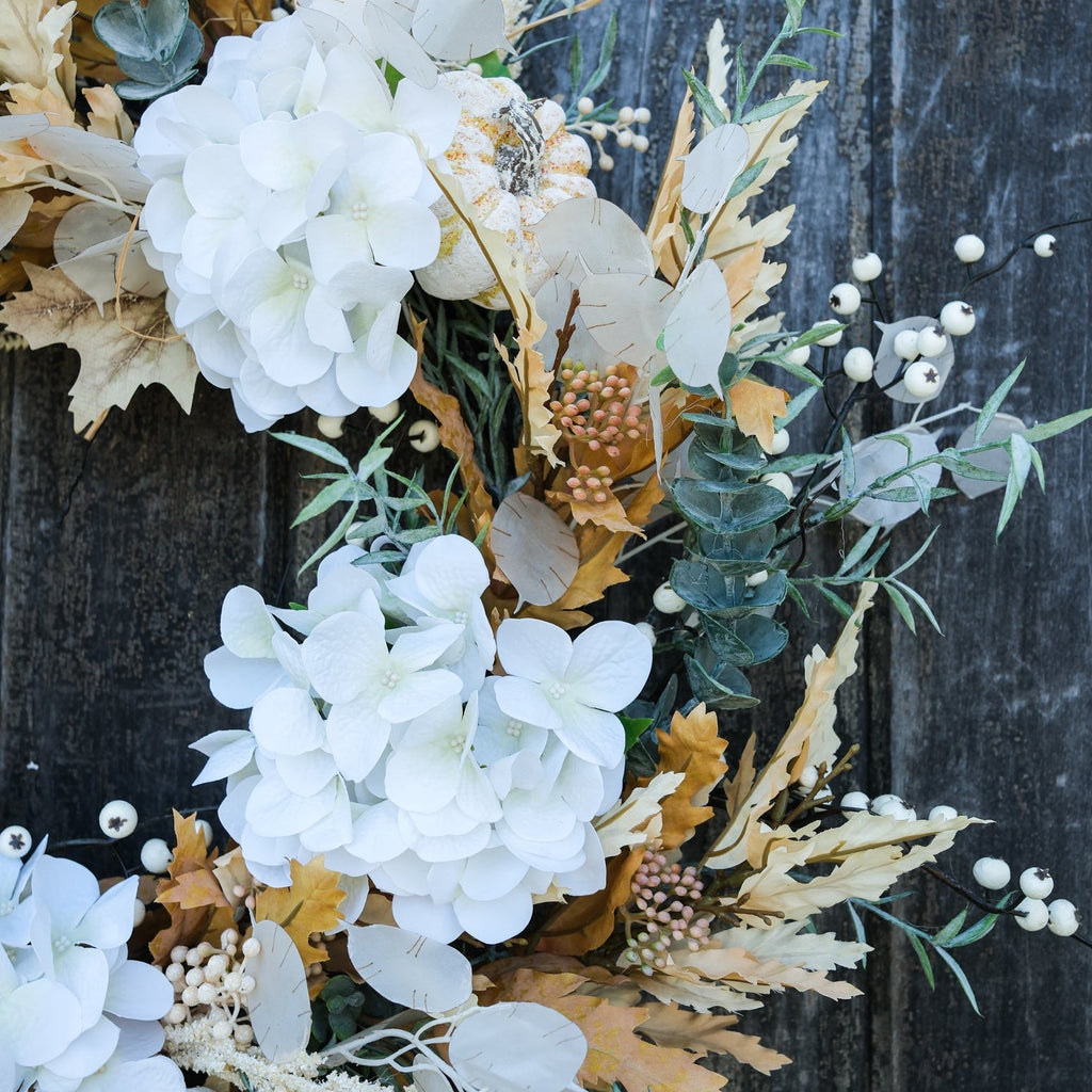 Truffle wreath close-up with layered white flowers, gold leaves, eucalyptus sprigs, and berries.