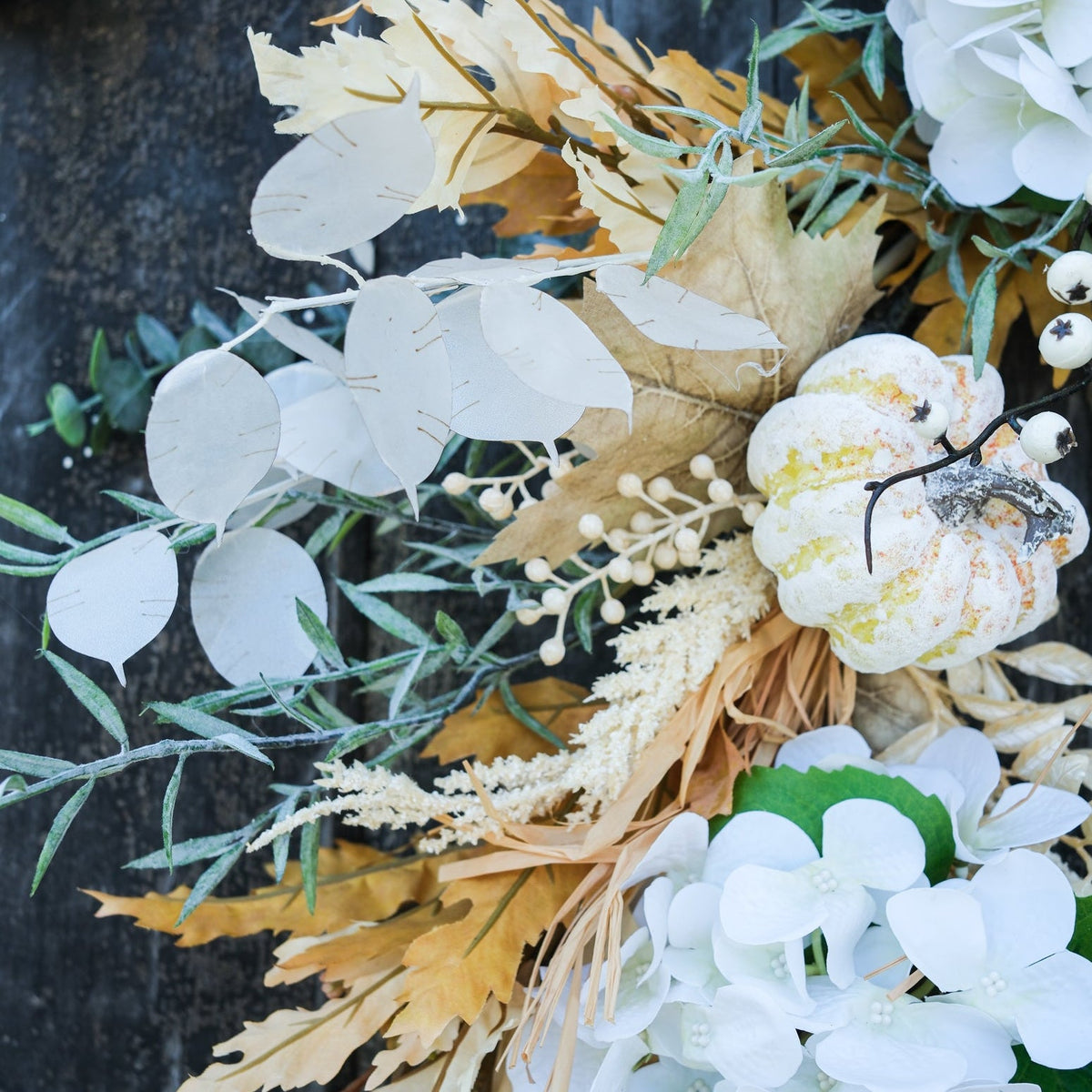 Truffle wreath detail showing white leaf accents, tan dried foliage, and pale gold berry ornaments.