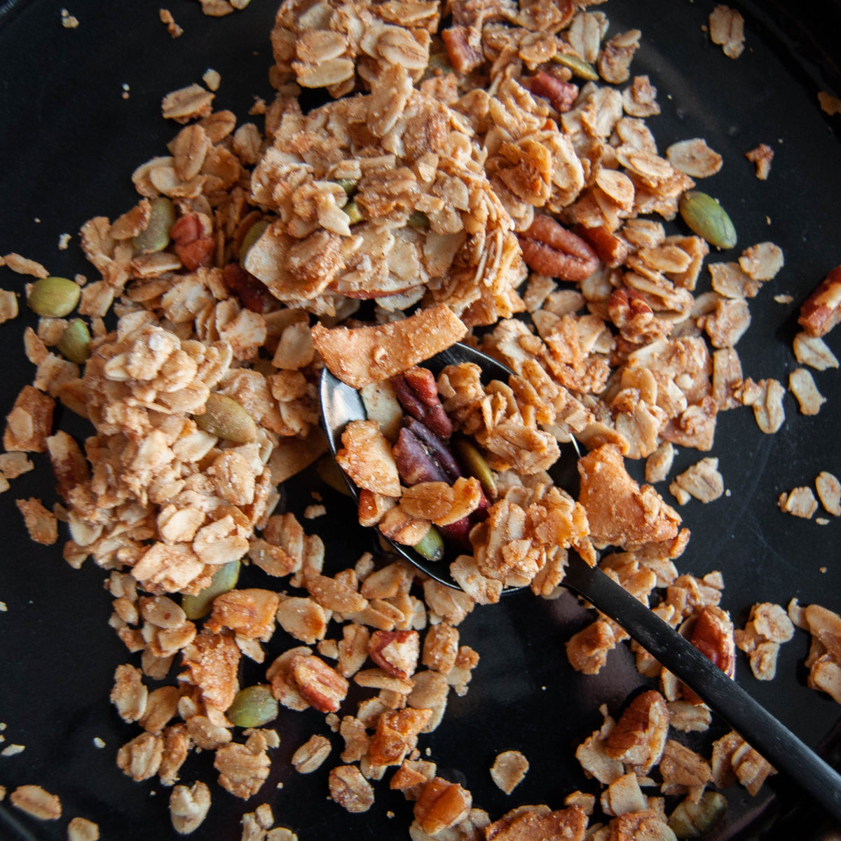 Maple pecan granola with sea salt, toasted oats and nuts scattered on a dark tray