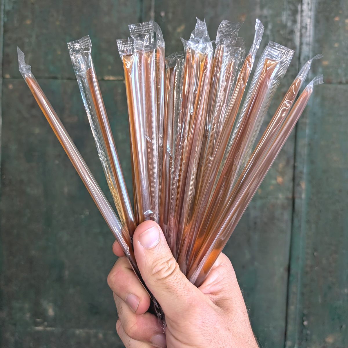 Hand holding multiple honey sticks in mixed amber and brown shades, in wrappers
