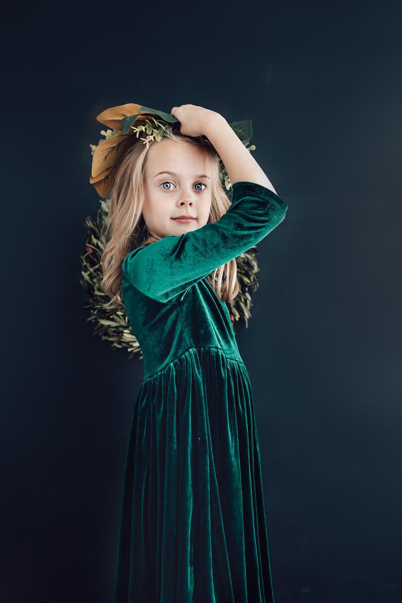 Dark green velvet long-sleeve twirl dress with gathered skirt, child standing sideways