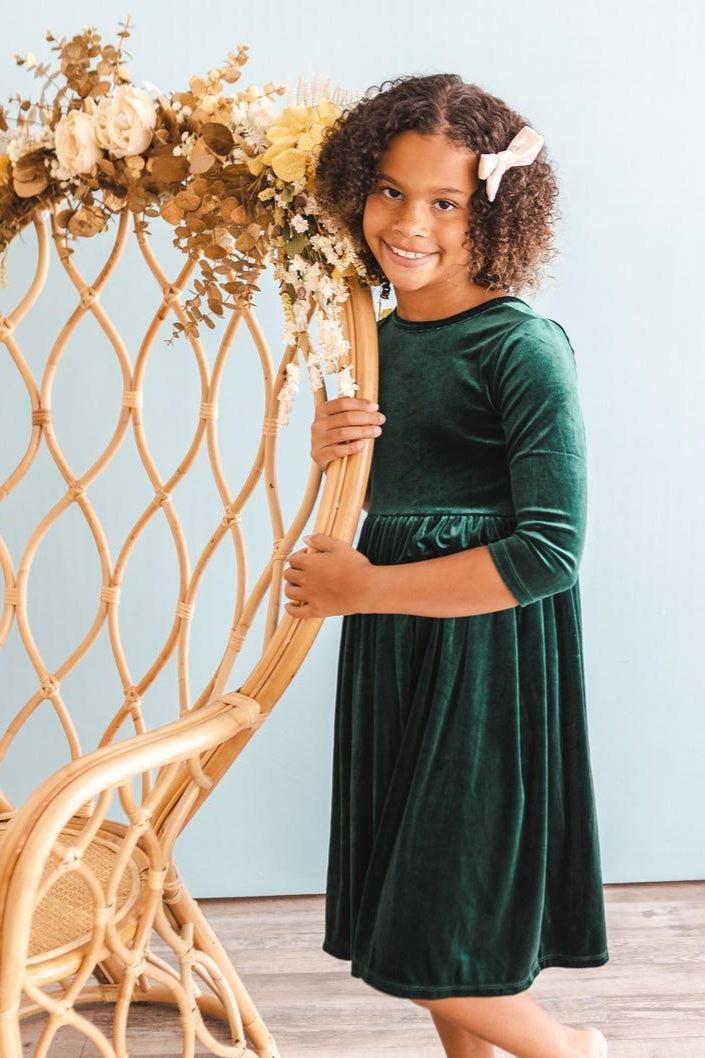 Dark green velvet twirl dress with long sleeves and gathered waist, child posing