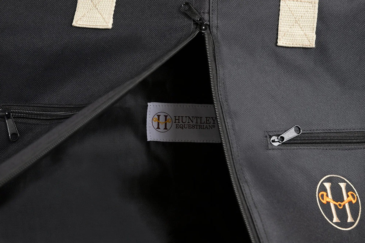 Close-up of black garment bag interior with zipper, Huntley Equestrian label, and logo