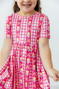 Girls pink plaid twirl dress with tulip and bow print, short sleeves, gathered skirt