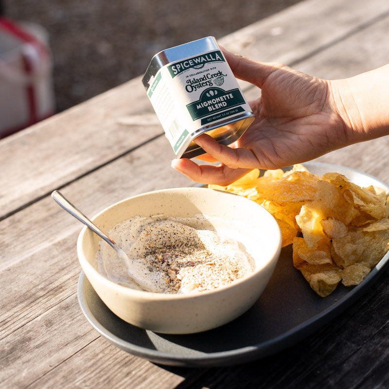 Hand holding SpiceWalla mignonette blend tin over bowl and crackers on plate