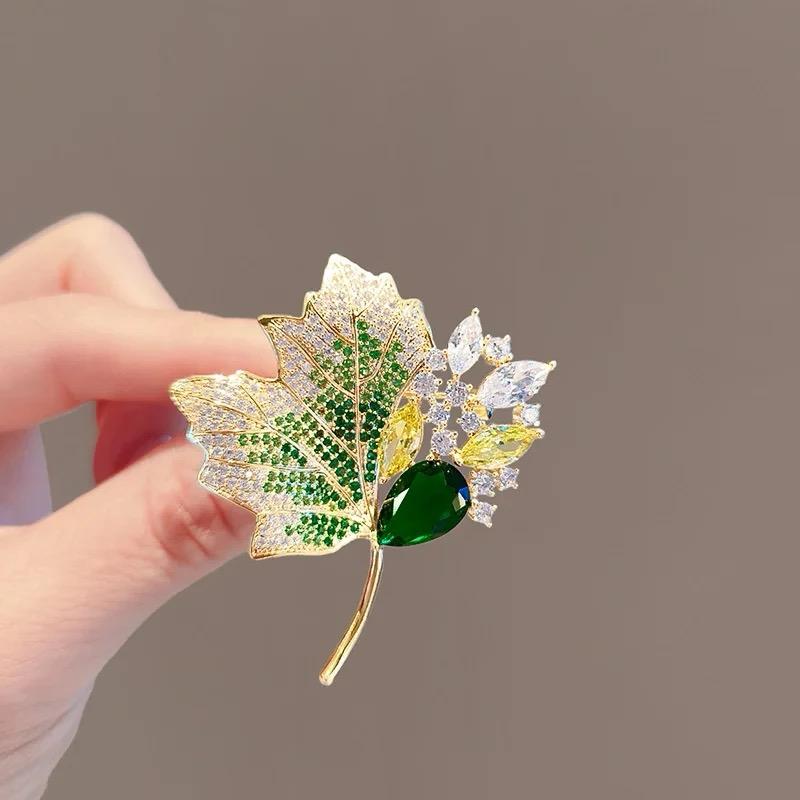 Gold-tone autumn foliage brooch with green center gem, white accents, and leaf-cut crystal details