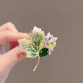 Gold-tone autumn foliage brooch with green center gem, white accents, and leaf-cut crystal details