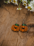 Pumpkin-shaped dangling earrings with green stems and black heart cutouts