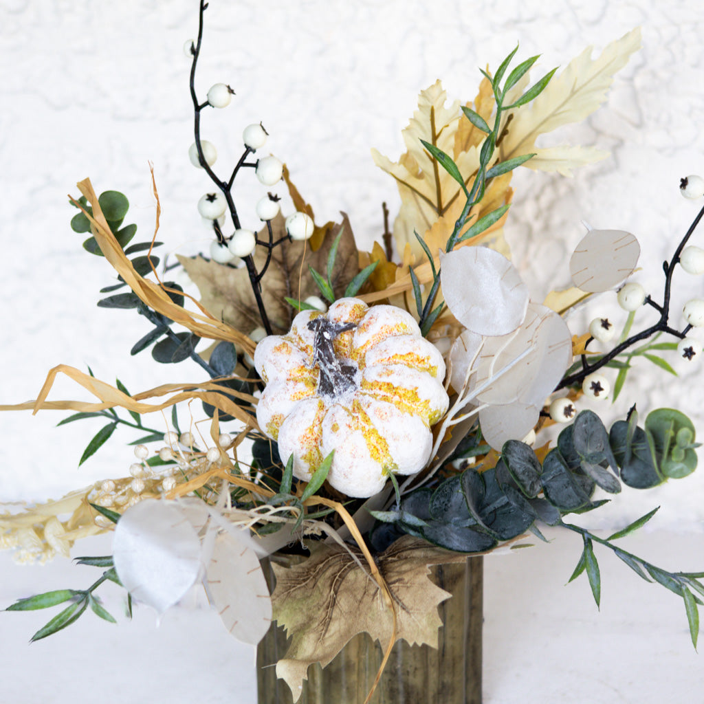 Floral arrangement with white and gold-speckled bloom, leafy greens, and pale leaf cutouts in vase