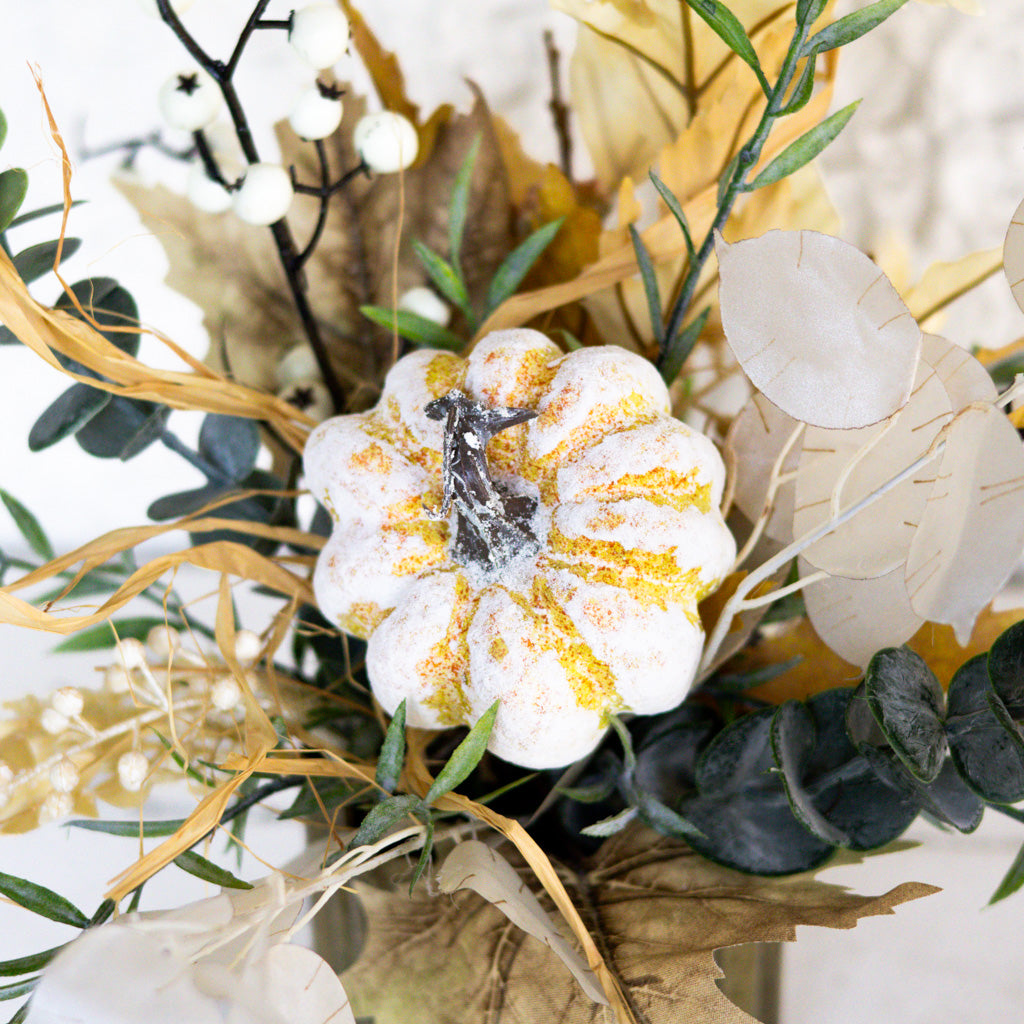 Macro view of white and gold-speckled flower with eucalyptus leaves and dried grasses in vase