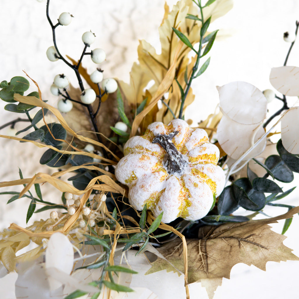 Close-up floral arrangement with white and gold-speckled flower, eucalyptus leaves, and dangling berries