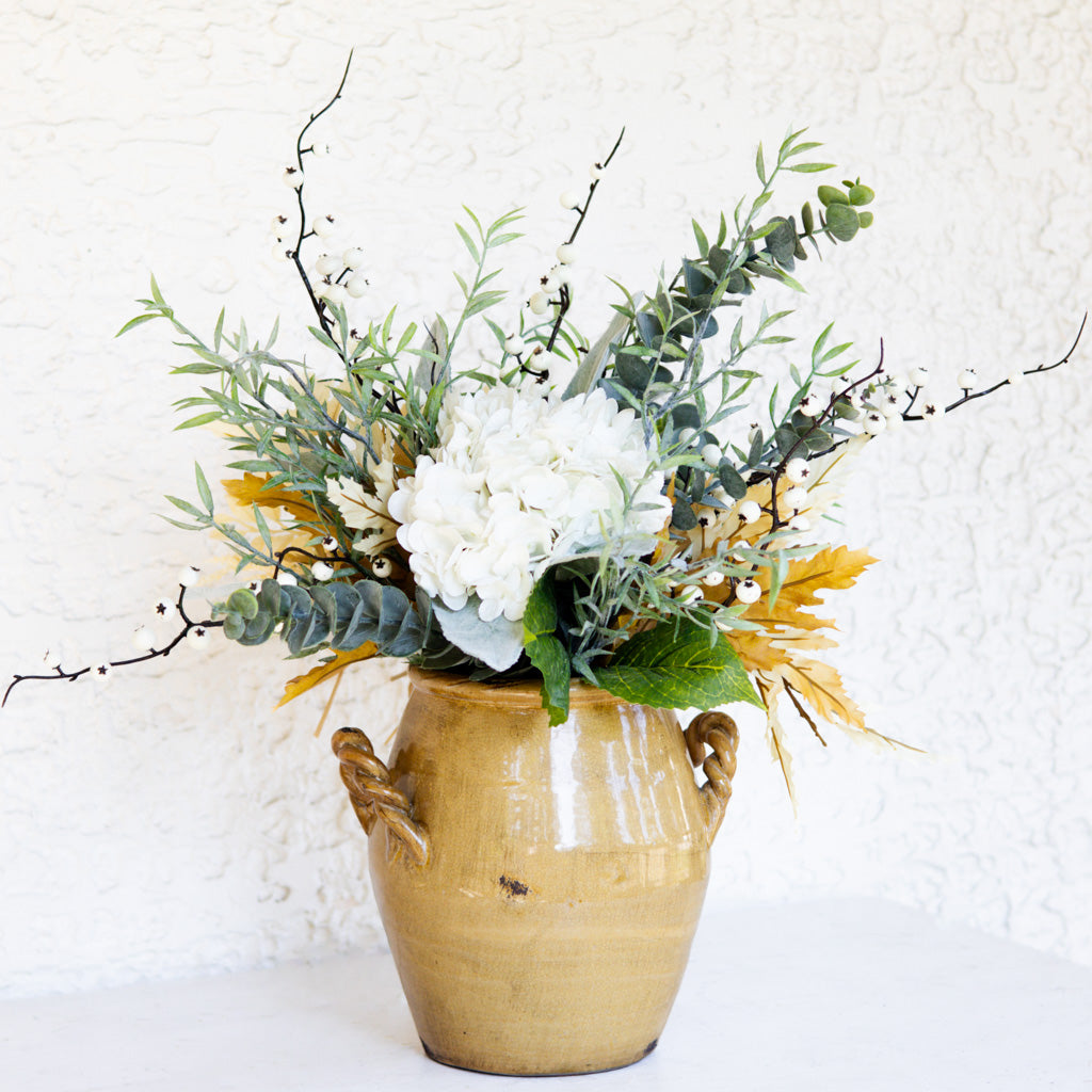 Floral bouquet in gold vase with white rose-style blooms, greenery, and berry twigs